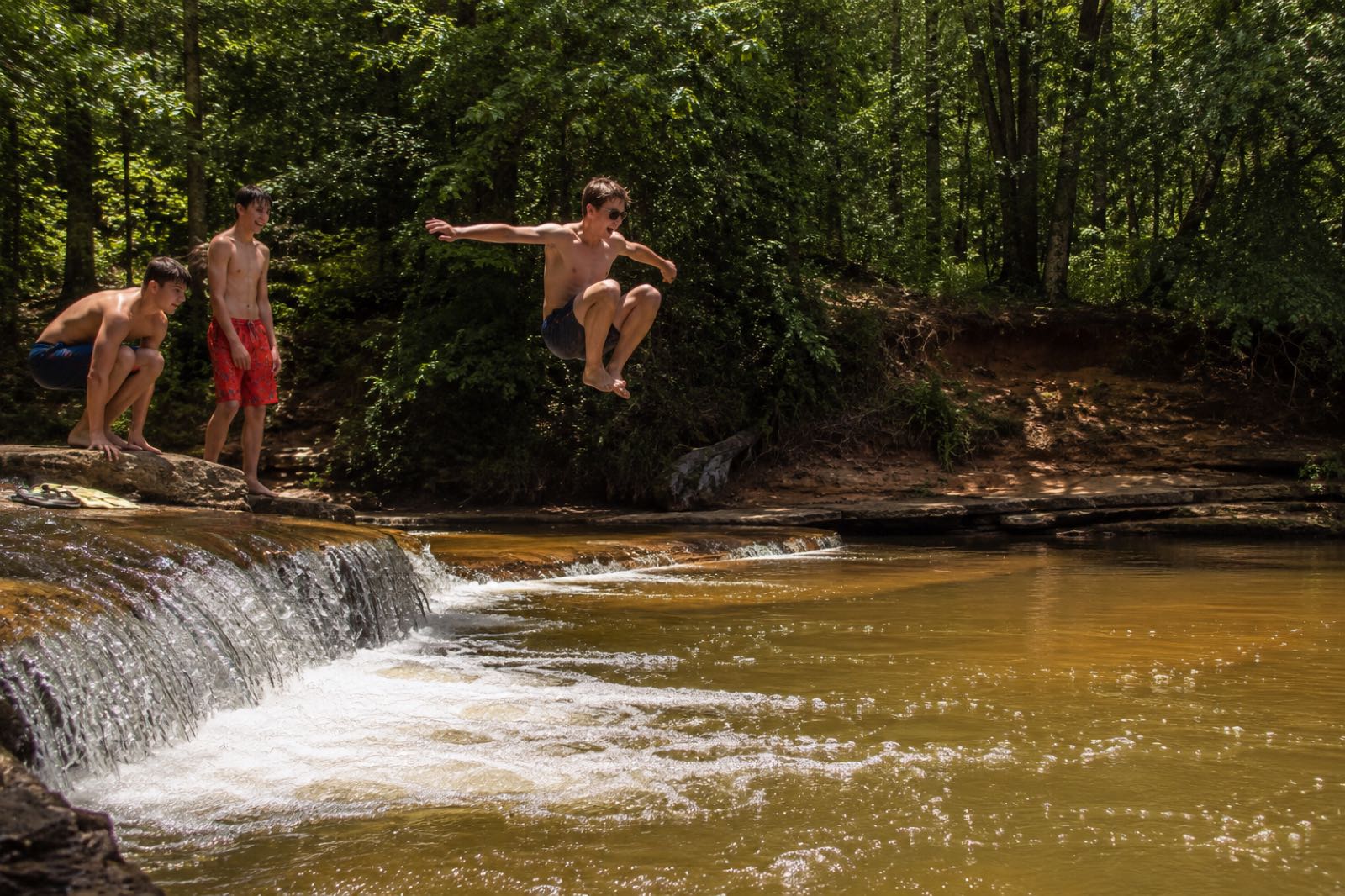 A swimmer jumping from a sandstone ledge into the pool below the falls
